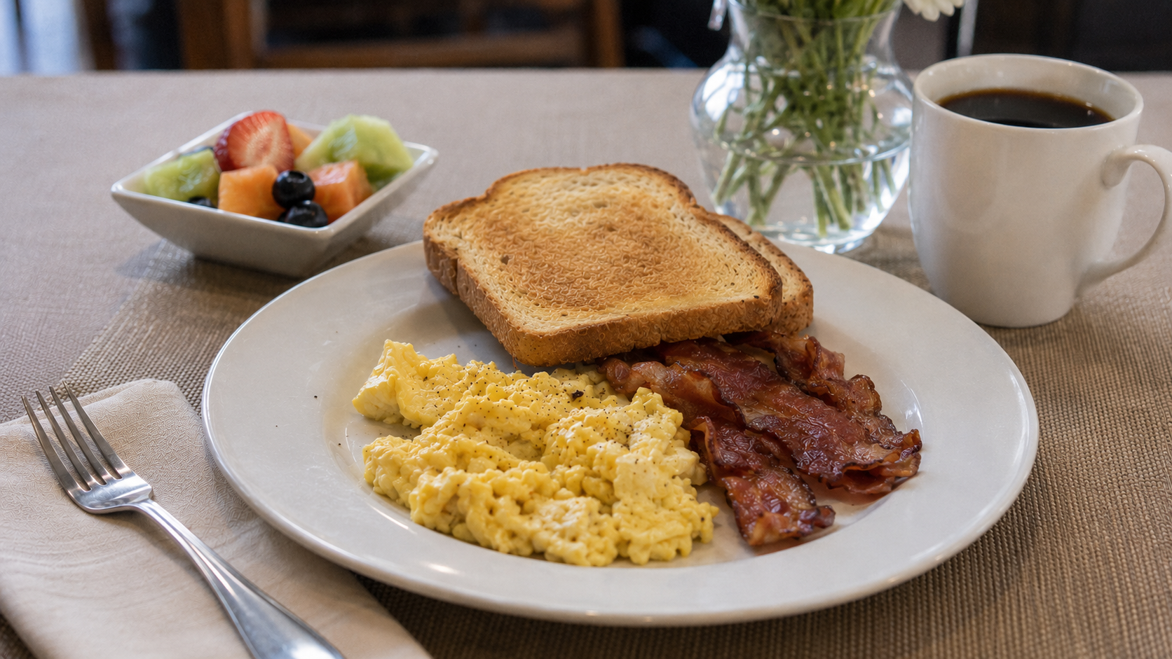Breakfast plate with eggs, bacon, toast, fruit and coffee